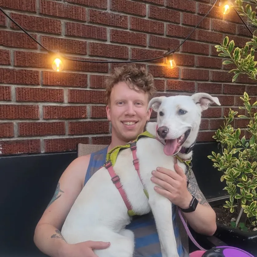 Colter Garrison holding his white dog Ožujsko under string lights
